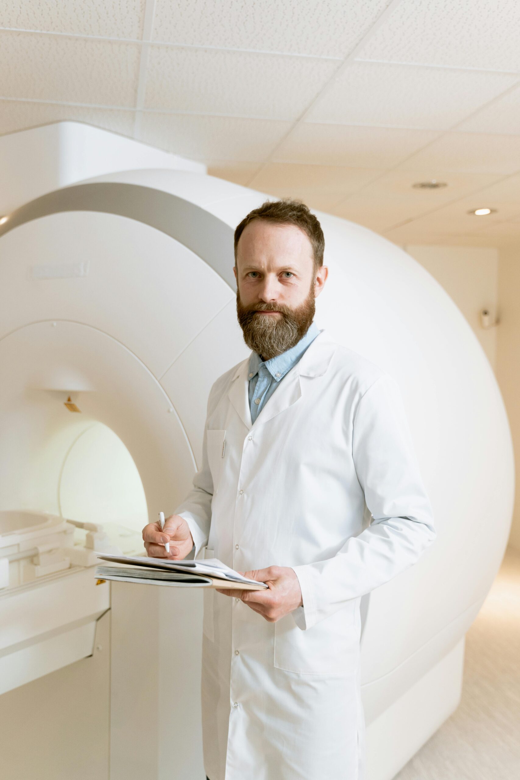 Radiology Manager dressed in white coat, writing on a clipboard next to an MRI machine.